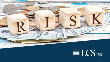 Wood letter blocks spelling out RISK laid on top of cash and coins