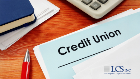 Blue folder labeled “Credit Union” on a wooden desk with papers, a pen, and a calculator, representing financial and compliance documentation.
